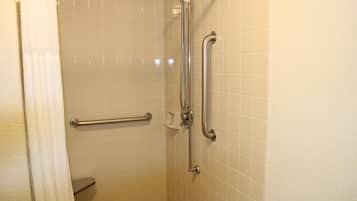A bathroom with white tiled walls, a shower with a handheld showerhead, and grab bars.