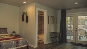 Ein Schlafzimmer mit einem Bett, einem kleinen Tisch, Stühlen, einer Dusche und einer Tür zu einer Terrasse.