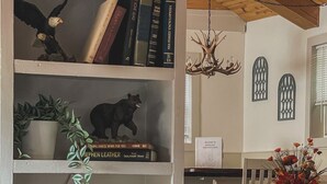 Ein gemütliches Wohnzimmer mit Bücherregal, einem Essbereich mit Tisch und Stühlen sowie einer Deckenleuchte.