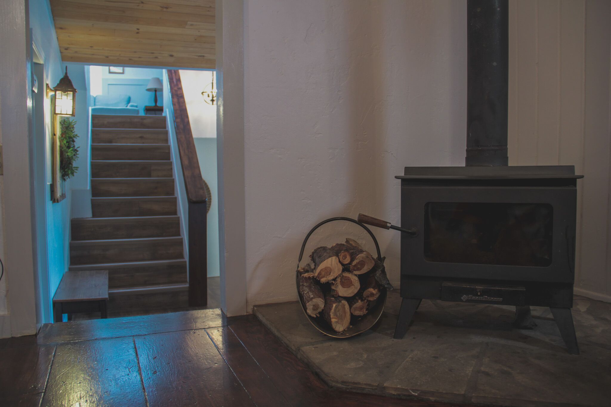 Un escalier menant à un deuxième étage, un poêle à bois et un panier de bois de chauffage.