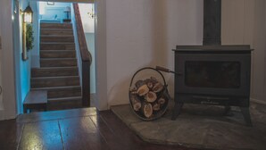 Eine Treppe führt zu einer zweiten Etage, ein Kaminofen und ein Holzscheitkorb sind zu sehen.