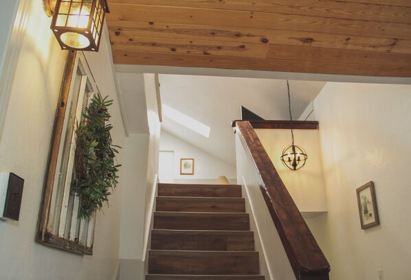 Un escalier en bois avec une rampe, une plante suspendue et un luminaire fixé au mur.