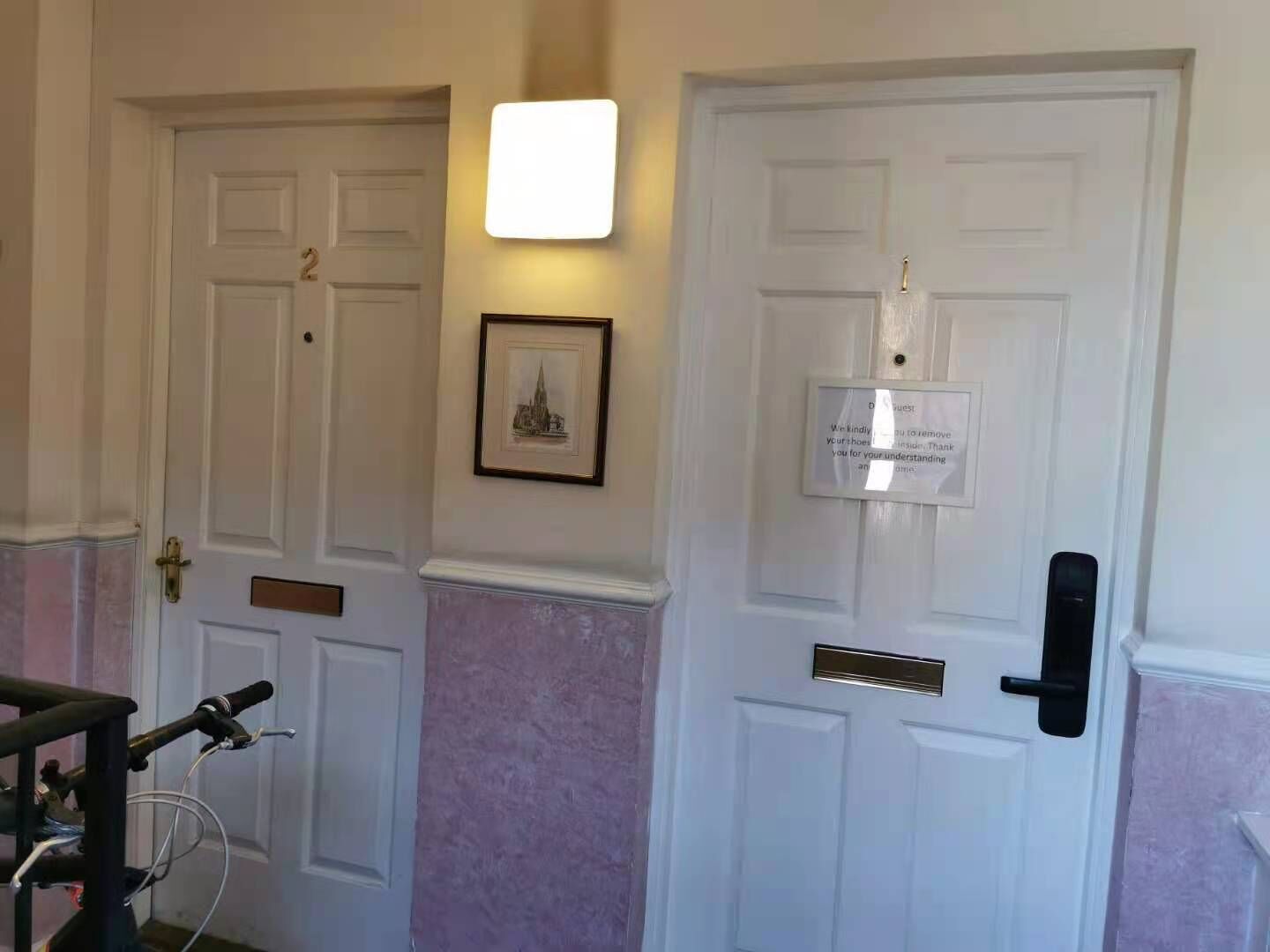 Ein Flur mit zwei weißen Türen, eine mit Schild und Beschilderung, und einem gerahmten Bild an der Wand.