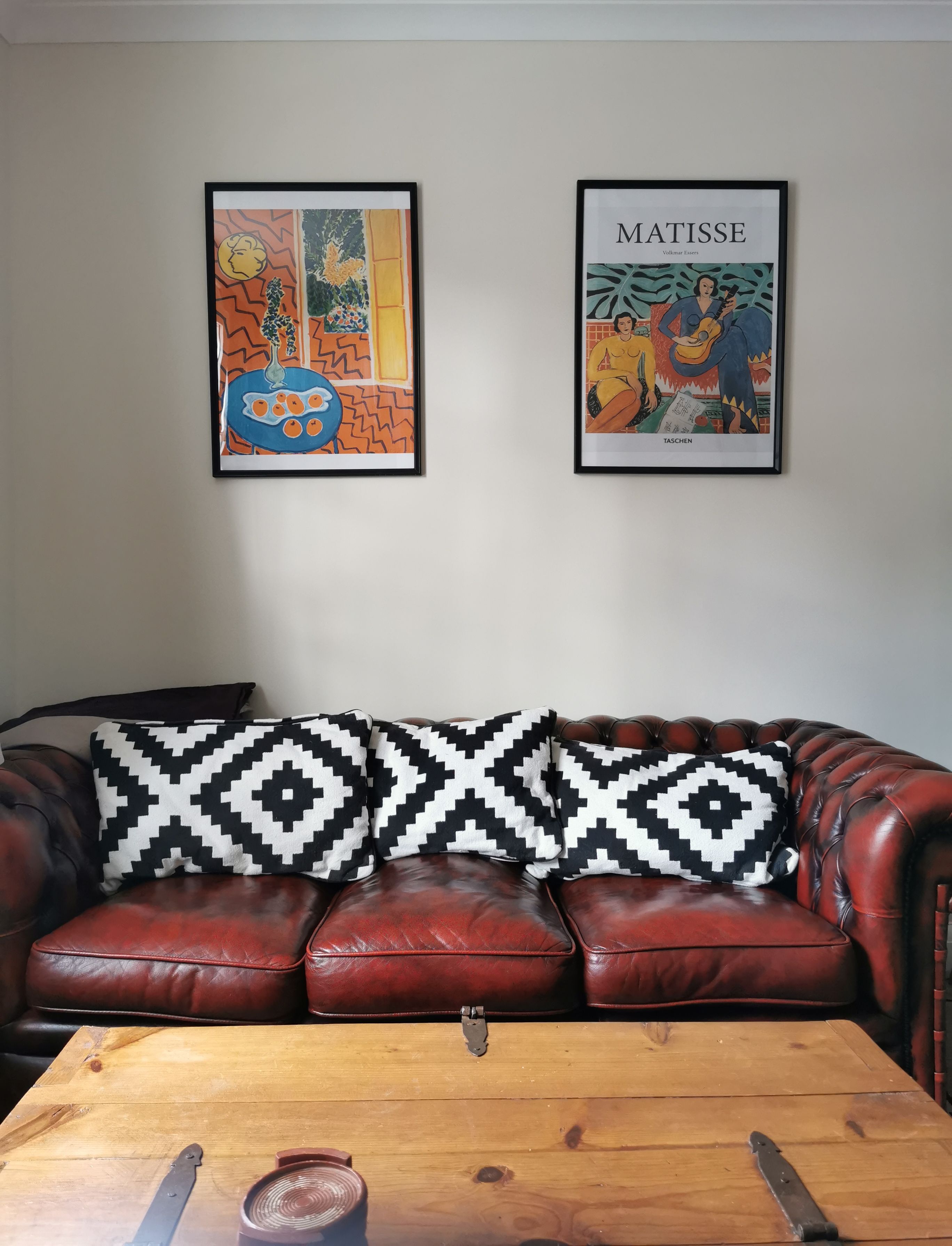 Una habitación con un sofá de cuero marrón, una mesa de centro de madera y dos obras de arte enmarcadas en la pared.