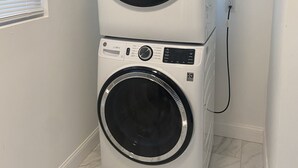 Un appareil combiné lave-linge et sèche-linge, installé dans un coin, près d’une fenêtre et d’une prise de courant.