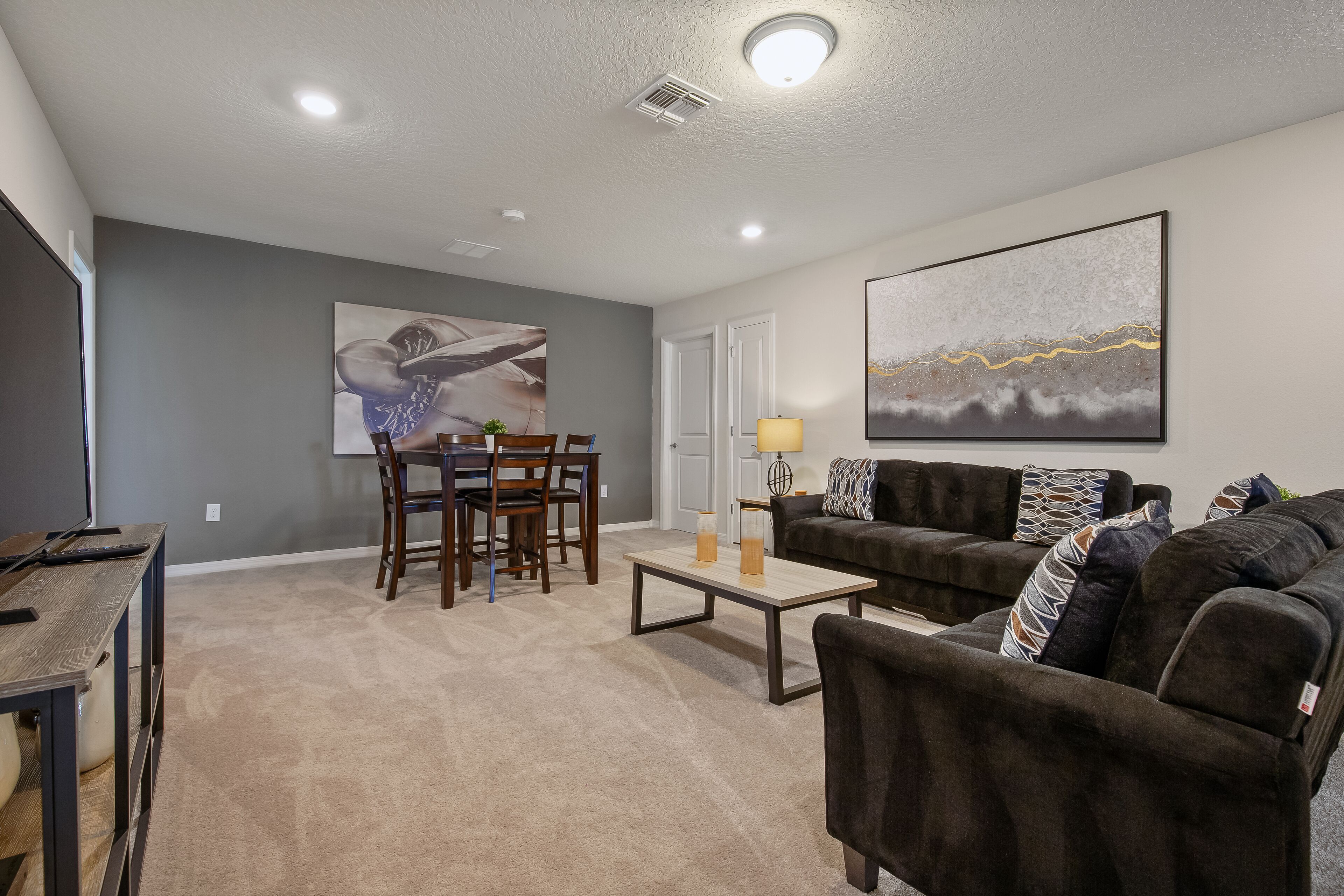 A living room with a dining area, a sofa, a coffee table, and artwork on the walls.