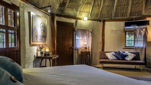 Quarto com cama, mesa de cabeceira, abajur, sofá e janela.