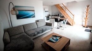 A modern living room with a grey sofa, a wooden coffee table, and a painting of a beach. - 3-star tourist DUPLEX SEA VIEW with Balcony & SWIMMING POOL (Penmarch)