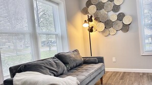 Un salón con un sofá gris, una manta blanca, una lámpara de pie y una pared decorada con platos redondos.