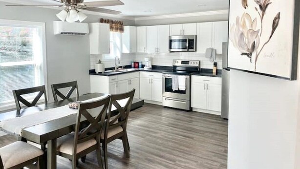 Una cocina moderna con armarios blancos, un microondas de acero inoxidable y un comedor con mesa y sillas.