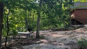 En rustik stuga med en träveranda och ett picknickbord i ett skogsområde.