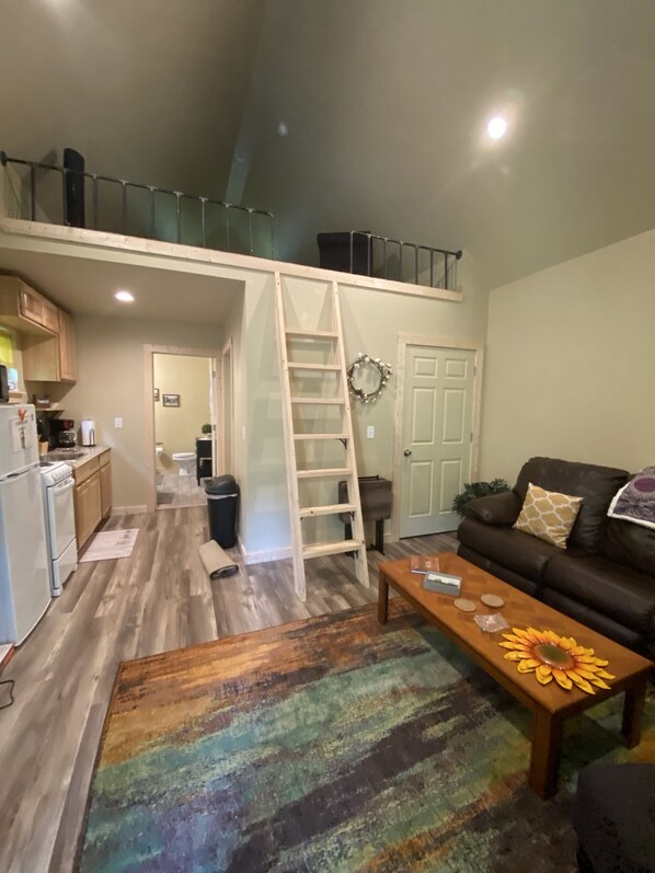 A loft-style living space with a kitchen, a wooden ladder, a couch, and a coffee table.