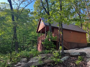 A cabin with a balcony, surrounded by trees and rocks.