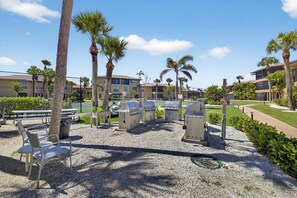 An outdoor patio area with barbecue grills, seating, and palm trees.