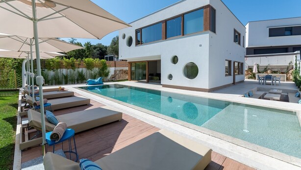 Une maison moderne à deux étages dotée d’une piscine, de chaises longues et de parasols.