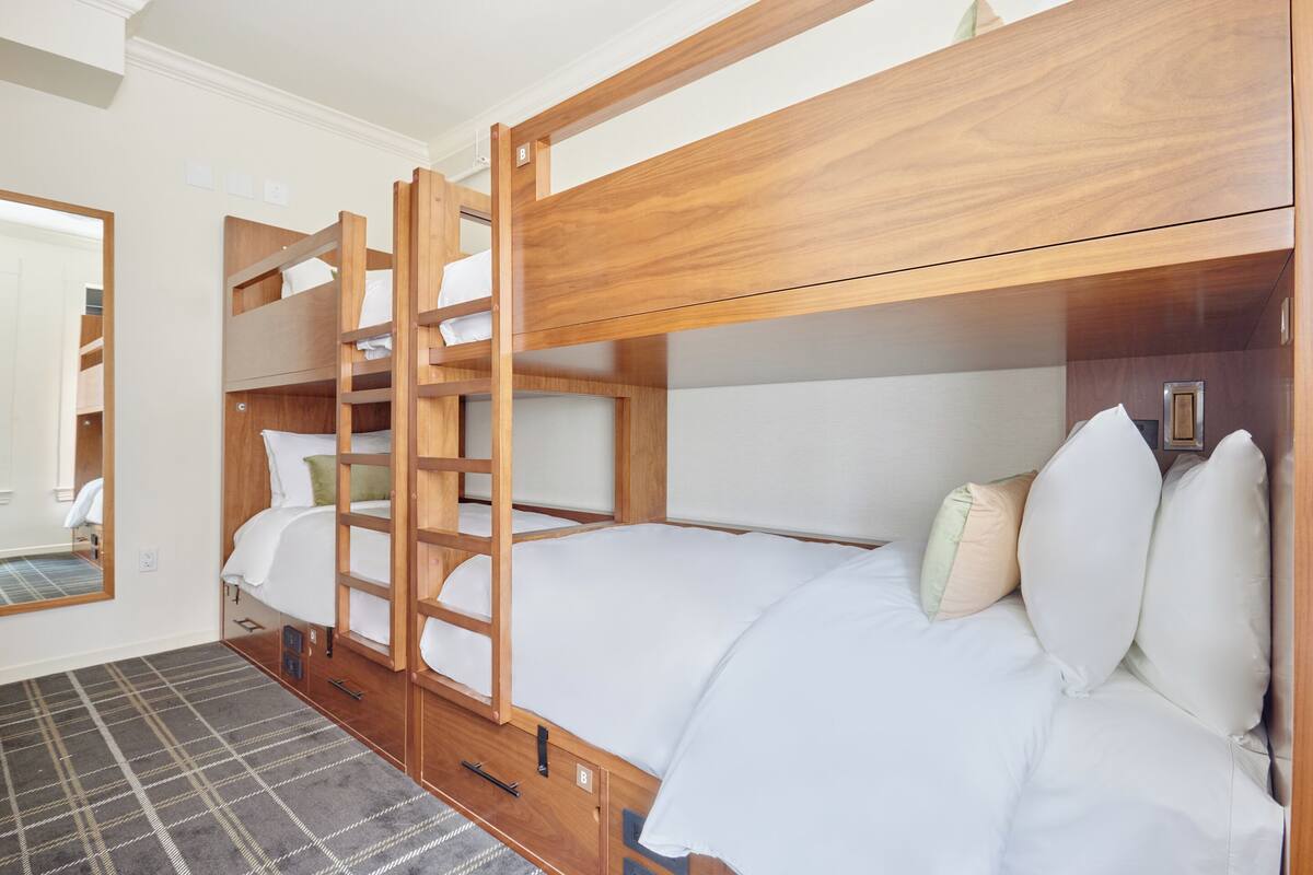 A bunk bed room with a wooden ladder, white bedding, and a plaid rug.