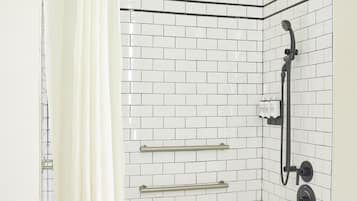 Ducha en esquina con paredes de azulejos blancos, una bañera blanca y un cabezal de ducha.