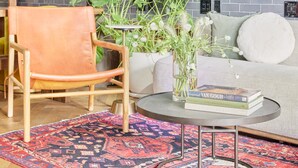 A modern living room with a grey brick wall, a round coffee table, a sofa, a leather armchair, and a patterned rug. - FOUND Hotel, San Francisco (San Francisco)