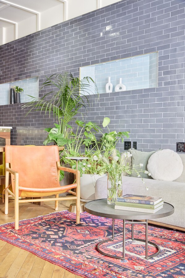 Un salon moderne avec un mur en briques grises, une table basse ronde, un canapé, un fauteuil en cuir et un tapis à motifs.