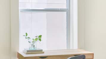 Une pièce avec un bureau près d’une fenêtre, une chaise et une petite plante sur le bureau.