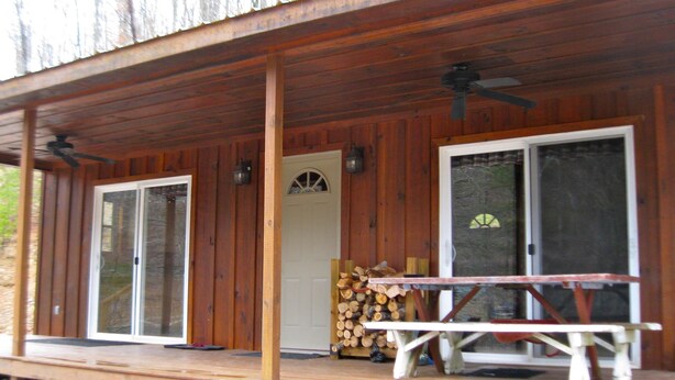Eine Holzveranda mit zwei Schiebegläsern, einer Bank und einem Holzstoß.