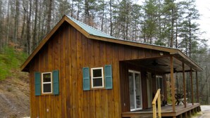 Eine Holzhütte mit Veranda, einer Tür und einer kleinen Sitzgelegenheit im Freien.