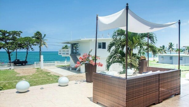 A beachside patio with a wicker sofa, a white canopy, and a view of the ocean. - LaCasita Ocean Front House (Aguada)