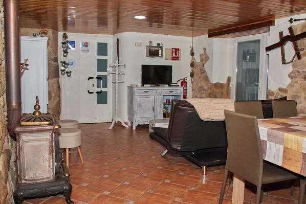 A dining area with a wooden table and chairs, a television, and a stone wall. - CORUXA HOUSE (San Salvador de Poio)