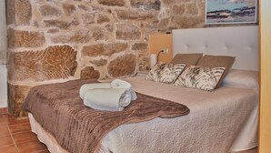 Un dormitorio con pared de piedra, una cama con manta y almohadas marrones, y un cuadro en la pared.