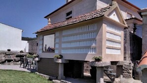 Un edificio con techo de tejas, un balcón con barandilla y un pequeño jardín con mesa y sillas.