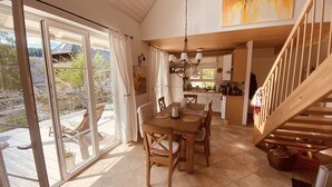 Et rummeligt køkken med træskabe, et spiseområde med et bord dækket til fire personer, og en trappe, der fører op til en etage.