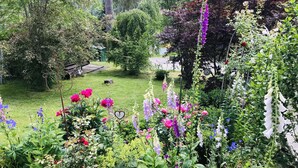 En frodig have med mange blomster og planter, en træbænk og en lille sø.