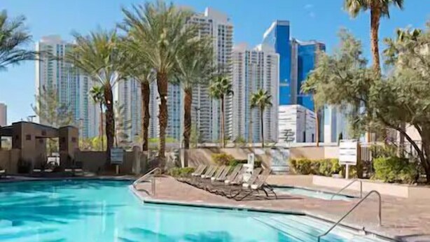 A swimming pool with lounge chairs, palm trees, and high-rise buildings in the background.