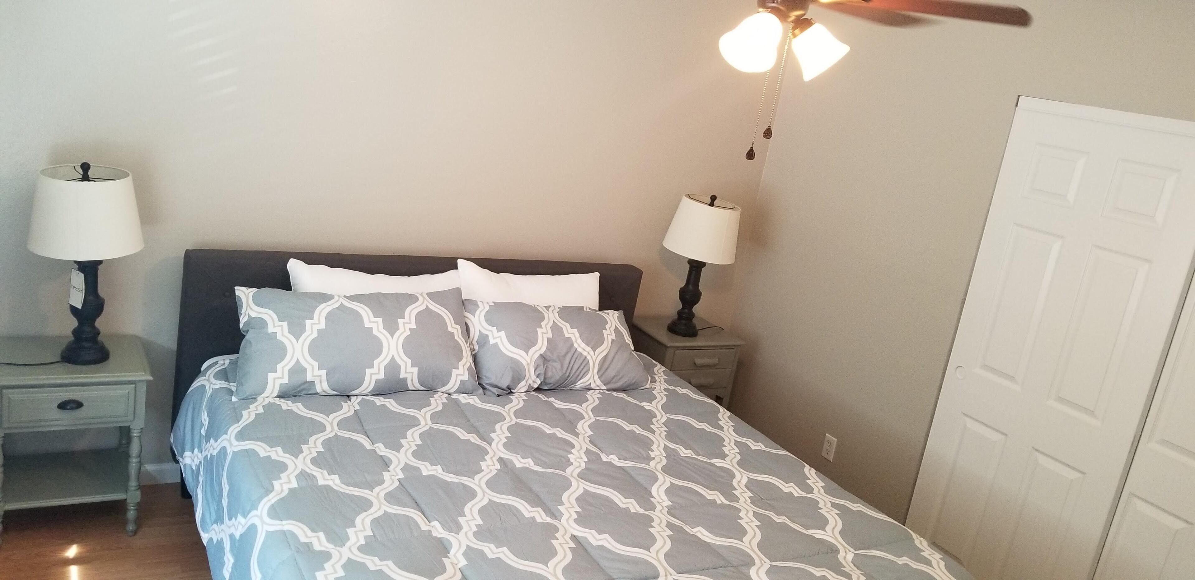 Une chambre à coucher avec un lit, deux tables de chevet, deux lampes, un ventilateur de plafond et une porte blanche.