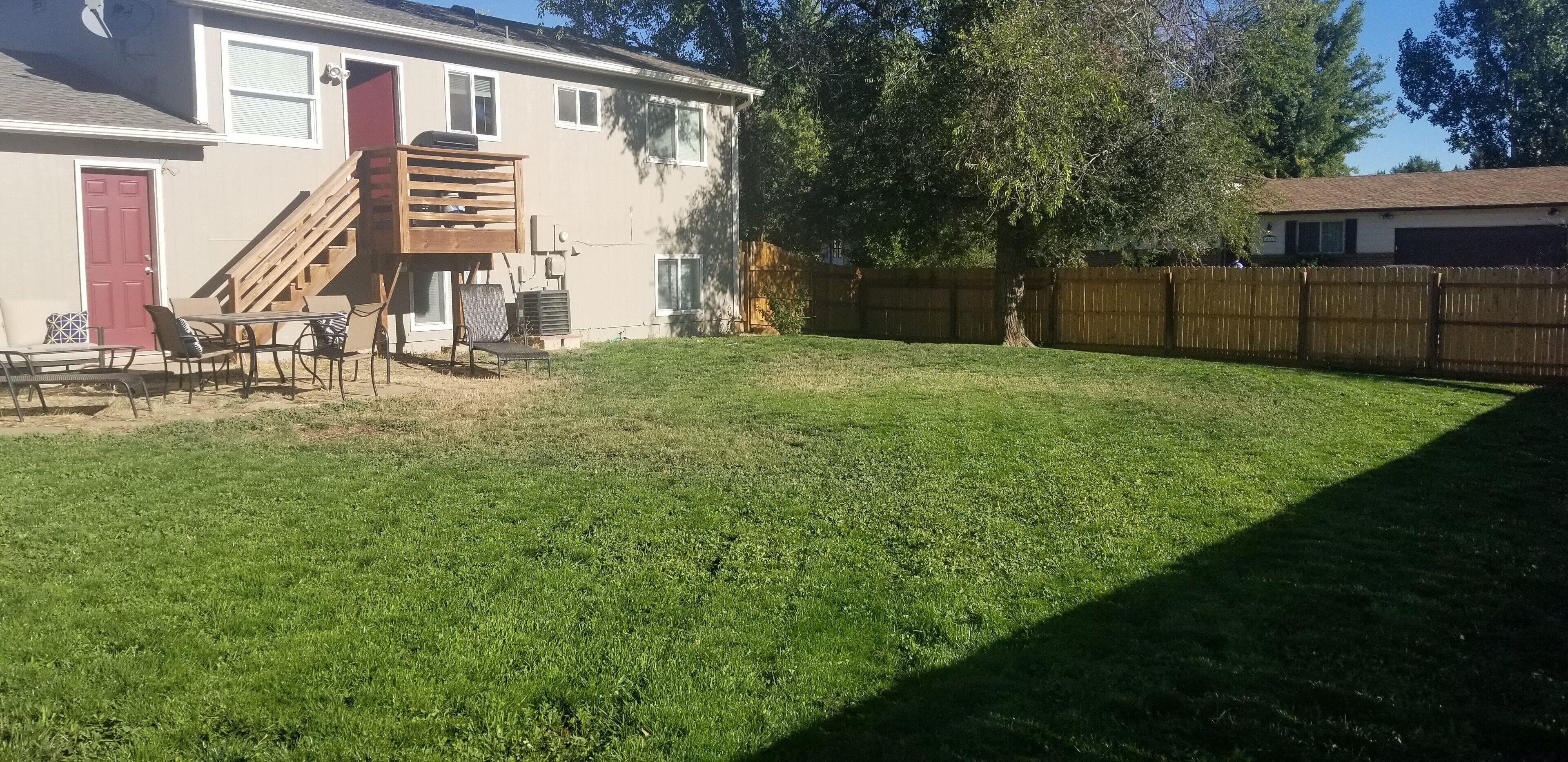 Ein Garten mit einer Holzterrasse, einer roten Tür und einem umzäunten Bereich.