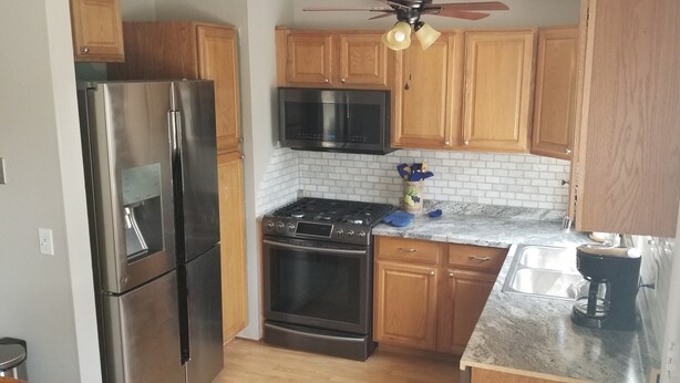 A compact kitchen with wooden cabinets, stainless steel appliances, a microwave, and a gas stove.