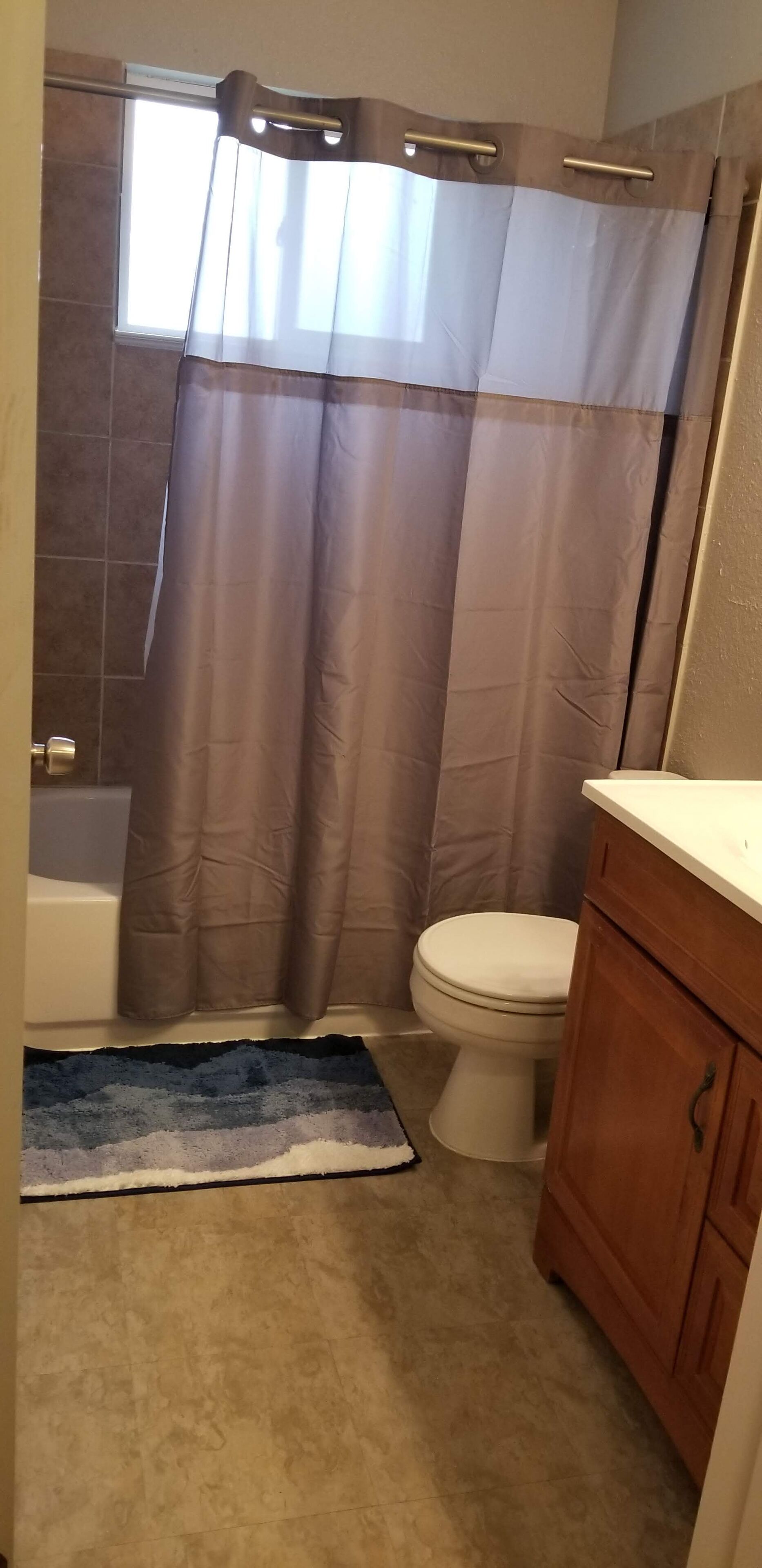 A bathroom with a shower curtain, a toilet, a bathtub, and wooden cabinets.