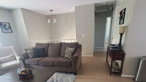 A living room with a brown sofa, a coffee table, and a patterned rug. There is a hallway leading to another room.