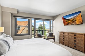 A bedroom with a large bed, a dresser, a chair, and a TV mounted on the wall.