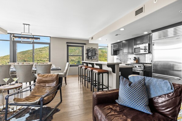 A modern kitchen with stainless steel appliances, a bar area with stools, and a dining area with leather furniture.