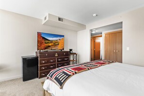 A bedroom with a bed, a dresser, a television on the wall, and a door leading to another room.