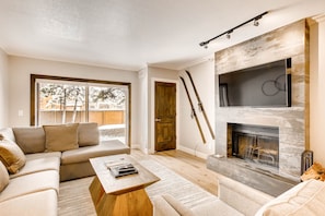 A modern living room with a sectional sofa, a wooden coffee table, a fireplace, and a large window offering a view of the outdoors. - Managed by Park City Lodging-Walk to Main Street and Town Lift on Free Shuttle (Park City)