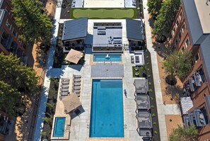 An aerial view of a residential building with a swimming pool, outdoor seating, and a tennis court.
