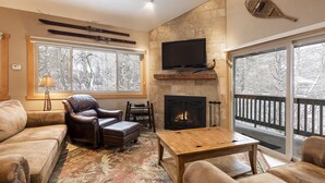 A cozy living room with a fireplace, leather armchair, and a large window with a view of snow-covered trees. - Managed by Park City Lodging-True Ski-In/Ski-Out to Park City Mountain Resort! (Park City)