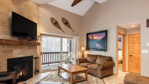 A cozy living room with a fireplace, leather furniture, a flat-screen TV, and a large window overlooking a snowy landscape. - Managed by Park City Lodging-True Ski-In/Ski-Out to Park City Mountain Resort! (Park City)
