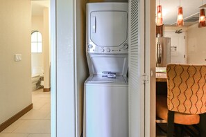 A compact, white washing machine in a narrow hallway with a toilet visible in the background. - Peoria | Spa Weekend | Pool + Spa (Peoria)