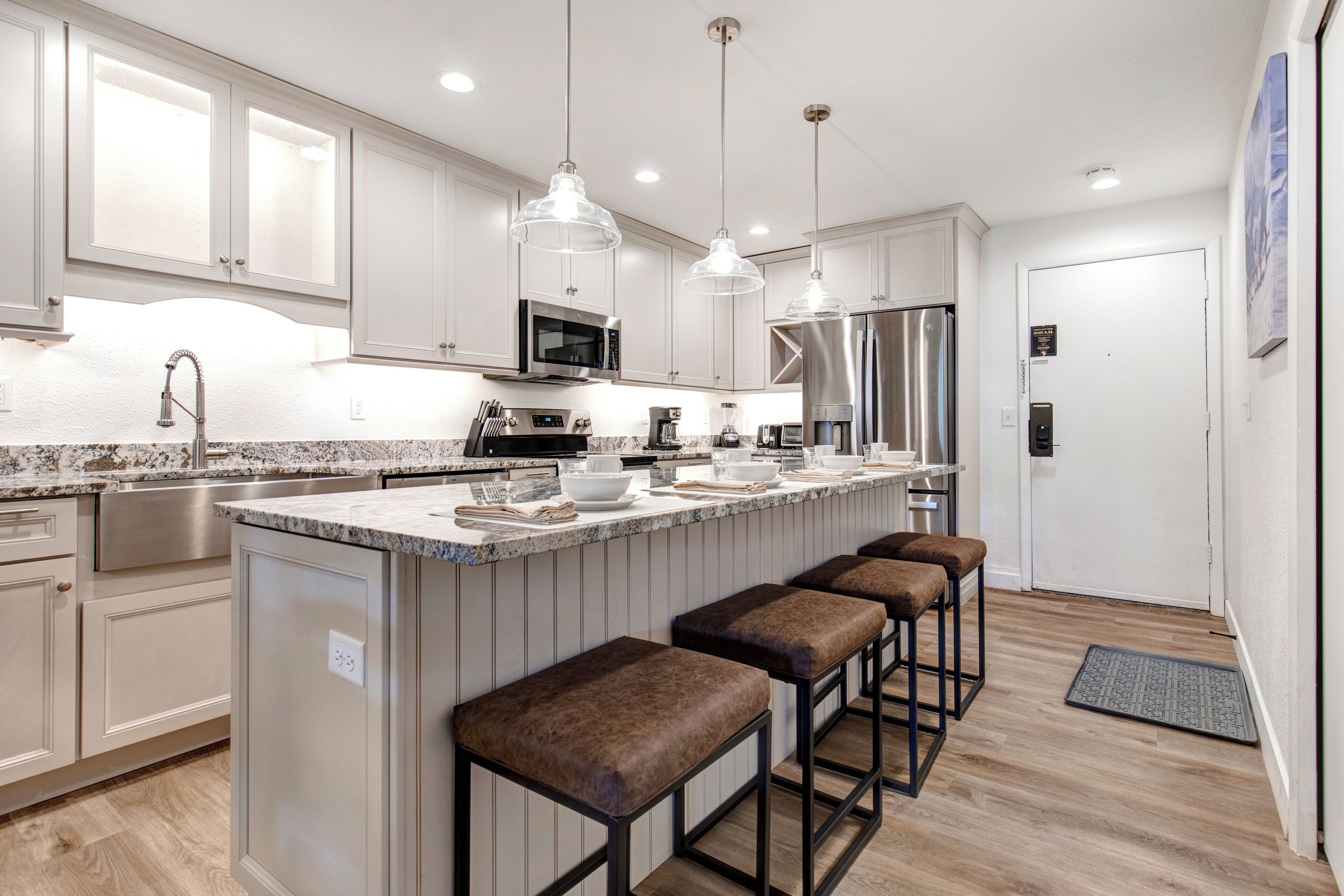 A modern kitchen with white cabinets, stainless steel appliances, a granite countertop, and bar stools.