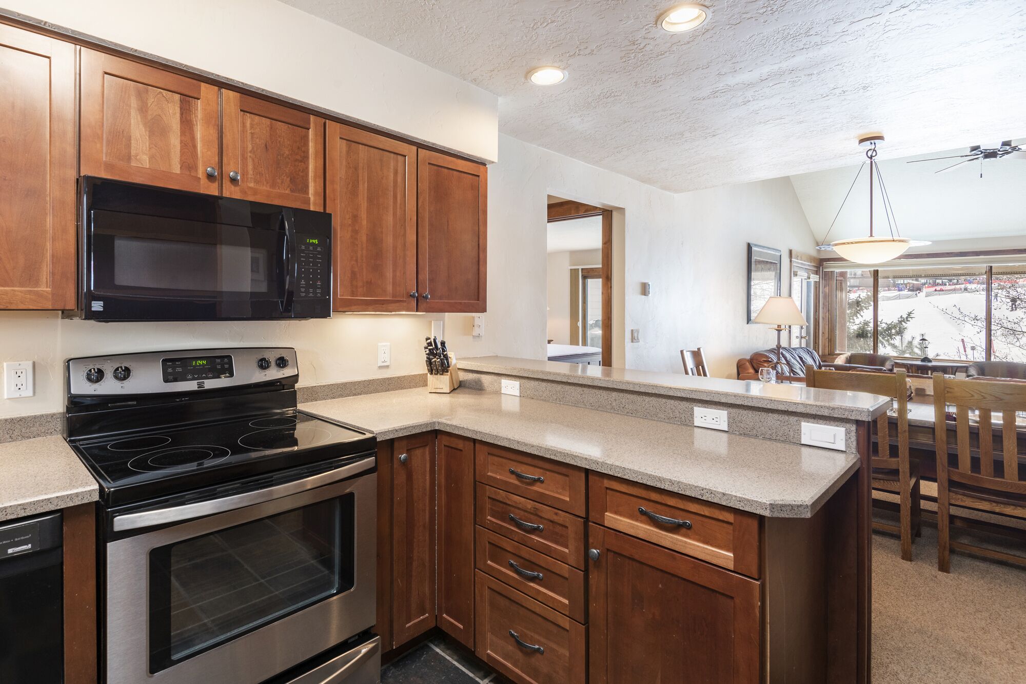A kitchen with wooden cabinets, a black microwave, a stainless steel stove, and a granite countertop.
