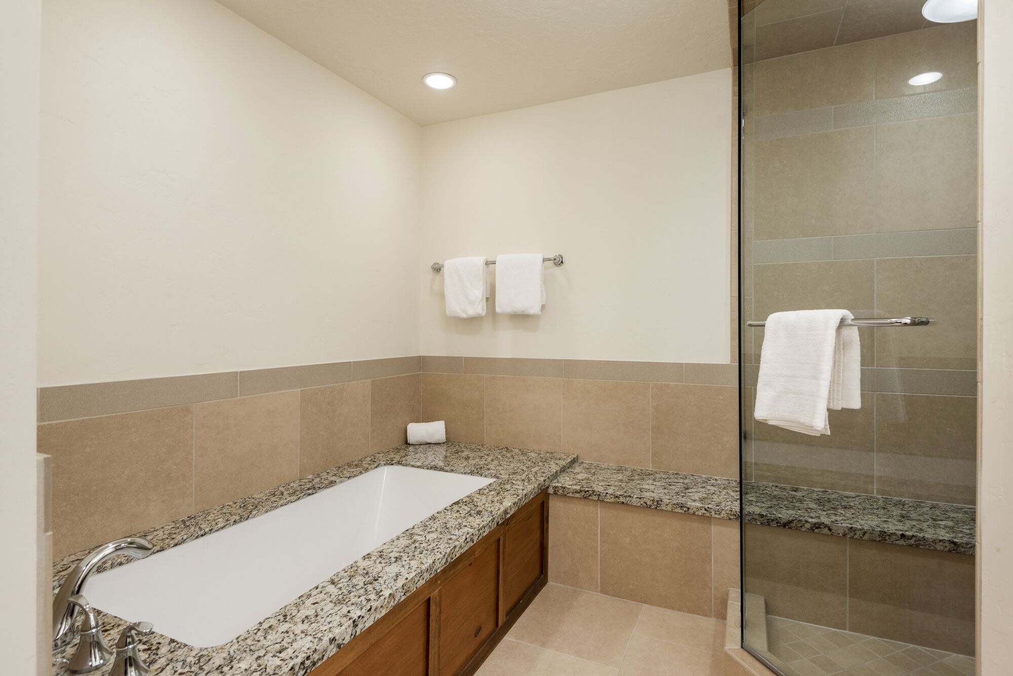Une salle de bain moderne avec un lavabo sur un plan de travail en granit, une douche en verre et des murs recouverts de carreaux beiges.