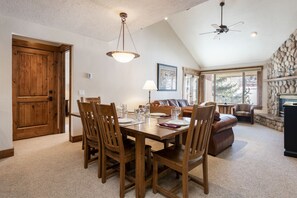 Uma sala de jantar com mesa e cadeiras de madeira, ventilador de teto e parede de pedra com lareira.